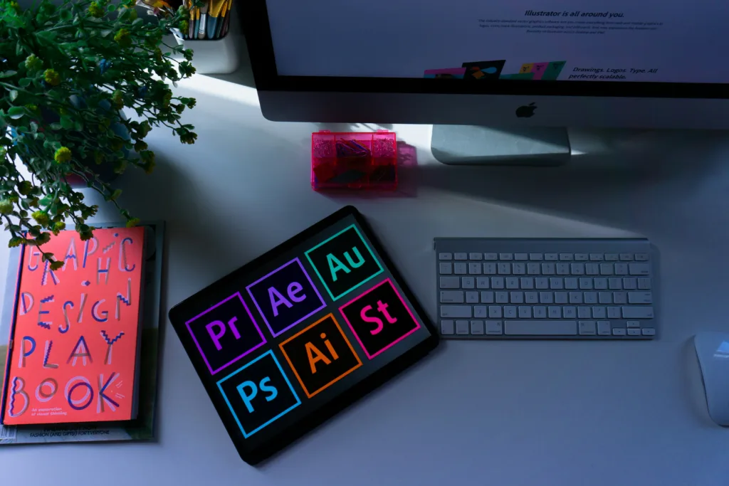 A rectangle of logos of the Adobe creative suite, with a computer next to it and a "Graphic Design Playbook" on a table.