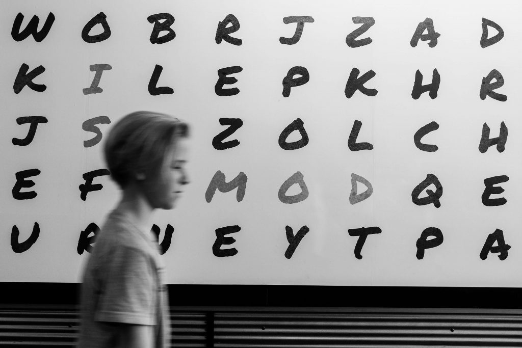 A young boy walking past a wall with random black letters on it