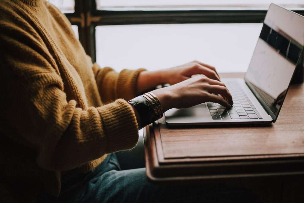 A person sitting at a desk at a Mac computer typing on the keyboard