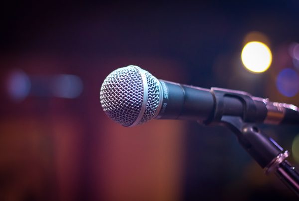 A microphone on a mic stand with a red curtain fuzzy in the background