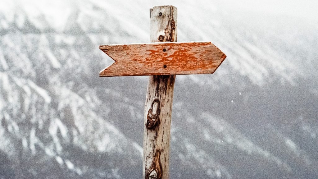 Wooden signpost with a wooden arrow facing to the right, with a snowy mountain scene in the background