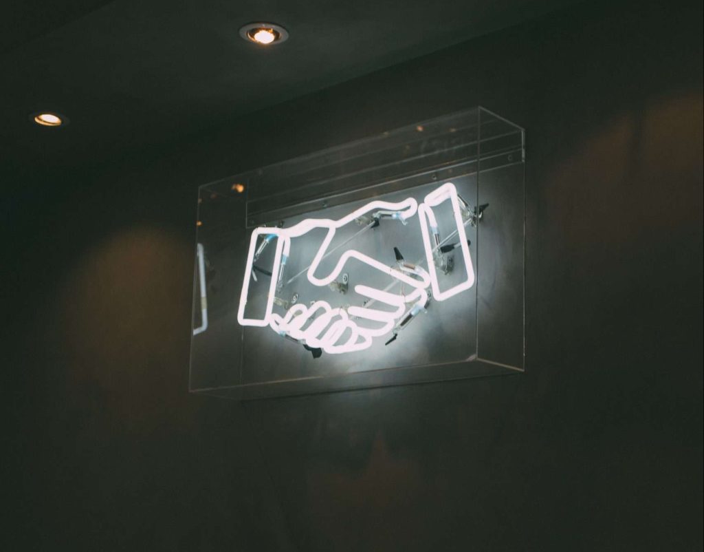 White neon sign with two hands in a handshake