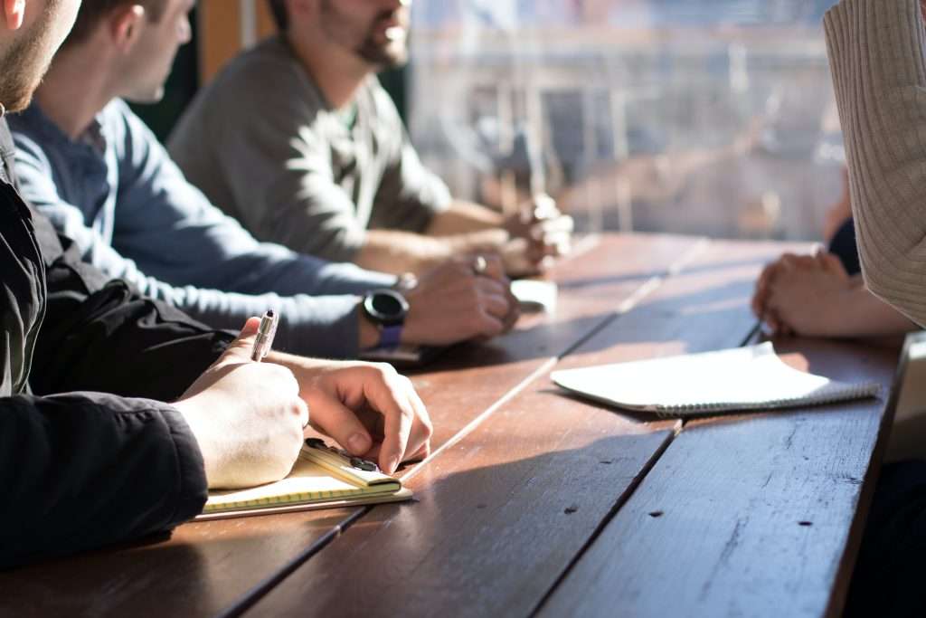 People gathered around a table writing on notepads