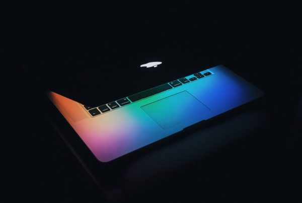 A half closed Mac computer with a rainbow of lights emitting from the screen