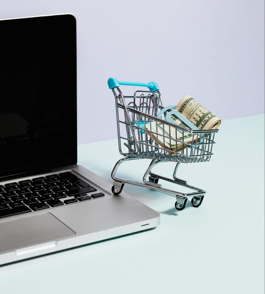 A small shopping cart with cash in it with one wheel on a laptop