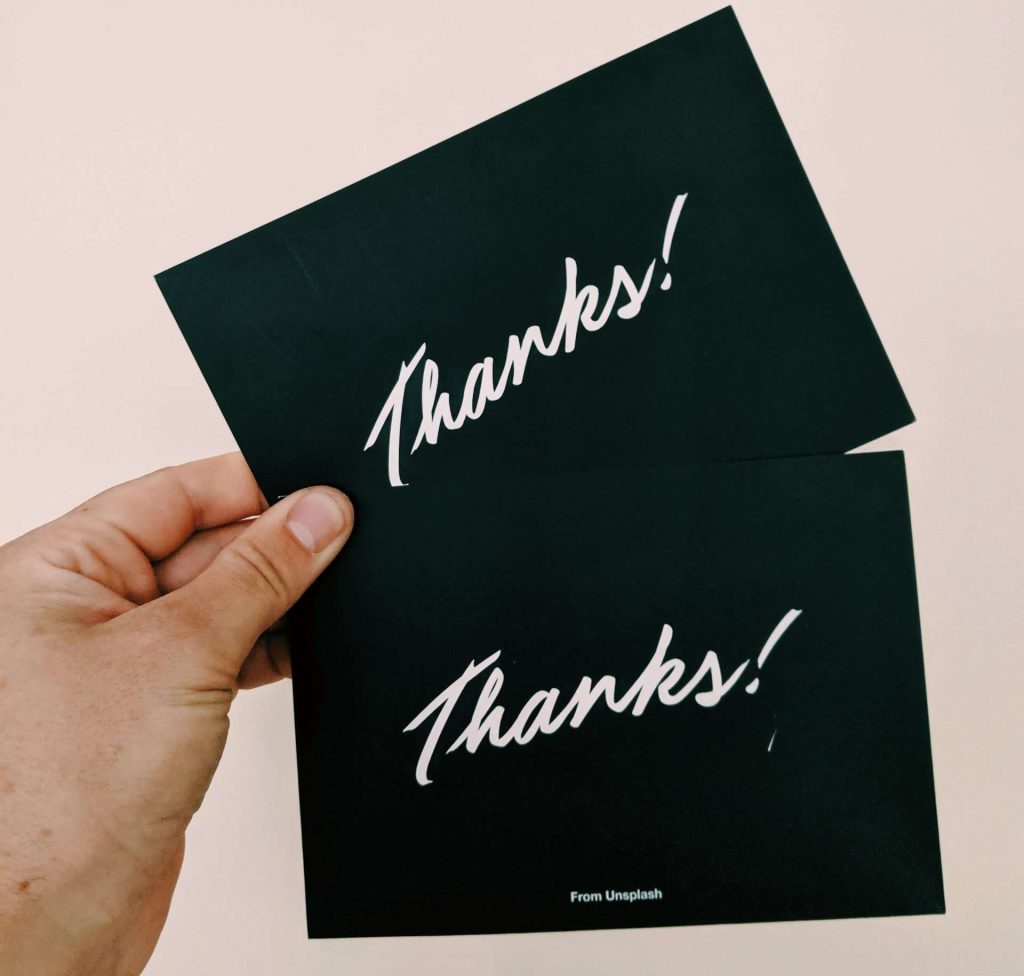 Person holding two black cards with white text saying "Thanks" in their left hand