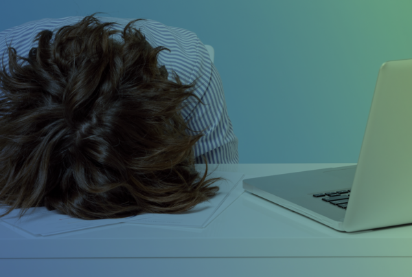 With a blue and green gradient background overlay, a person's head with brunette hair is face down on a table with a computer open on the person's left sid