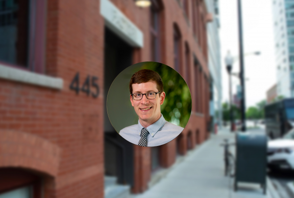 Circular headshot of Logical employee Ben Lippert with a faded background of Logical's brick office building