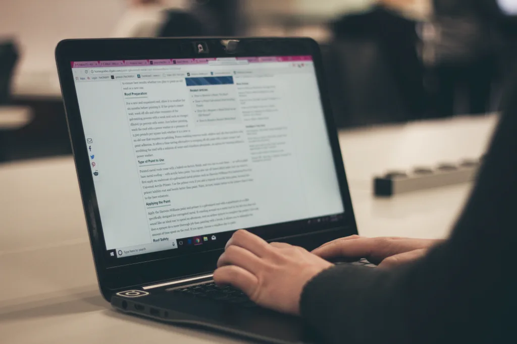 Person writing a blog on their laptop, which is placed on a wooden table