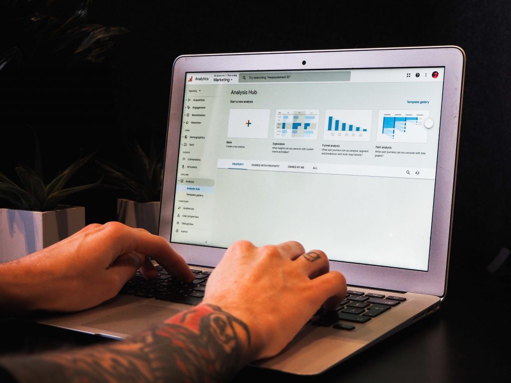 Person with tattooed arms typing on a Mac with GA4 showcased on the computer screen