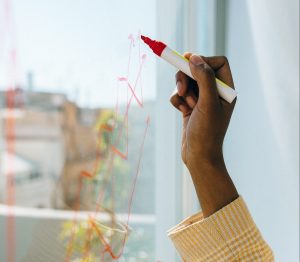 A person's hand writing with a red marker on a window