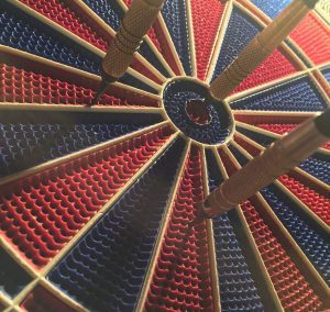 Black and red dart board with three darts on the board, one dart in the bullseye position
