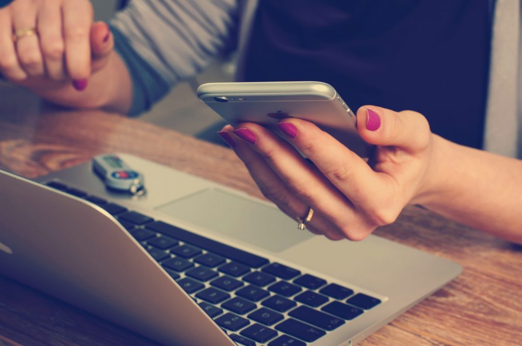 A woman’s hand holding a phone while on a computer